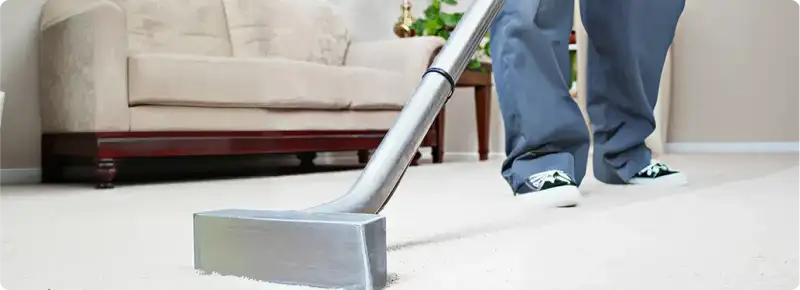 Carpet cleaning technician using a hot-water extraction wand on a light-colored carpet in a living room, Buffalo, NY.