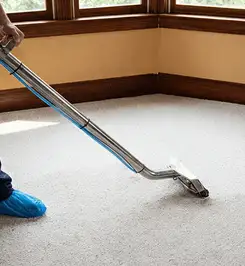 Steam carpet cleaning technician using a hot-water extraction wand on a residential carpet, wearing blue protective shoe covers Buffalo, NY.