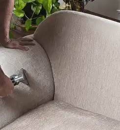 Professional upholstery cleaner deep-cleaning a fabric sofa with a handheld extraction tool and hose Buffalo, NY.