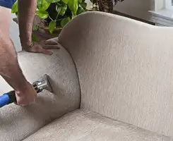 Professional upholstery cleaner deep-cleaning a fabric sofa with a handheld extraction tool and hose in Buffalo, NY.